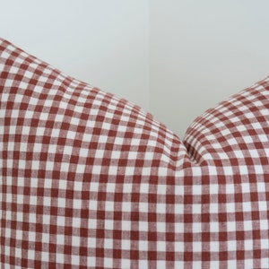 May include: A red and white gingham pillow cover. The pillow cover is made of a soft, woven fabric.