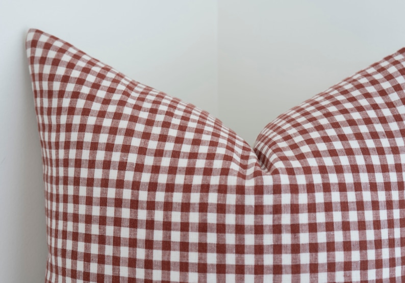 May include: A red and white gingham pillow cover. The pillow cover is made of a soft, woven fabric.