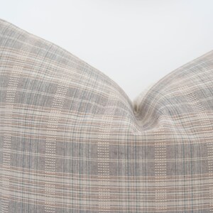 May include: A gray and beige plaid pillow with a subtle woven texture. The pillow is made of a soft, comfortable fabric and has a relaxed, casual look.