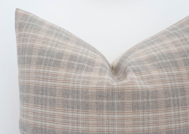 May include: A gray and beige plaid pillow with a subtle woven texture. The pillow is made of a soft, comfortable fabric and has a relaxed, casual look.