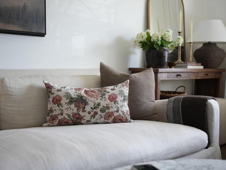 May include: A white linen sofa with a floral patterned cushion and a brown striped cushion. A brown throw blanket is draped over the arm of the sofa.