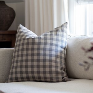 May include: A gray and white gingham throw pillow on a white couch.