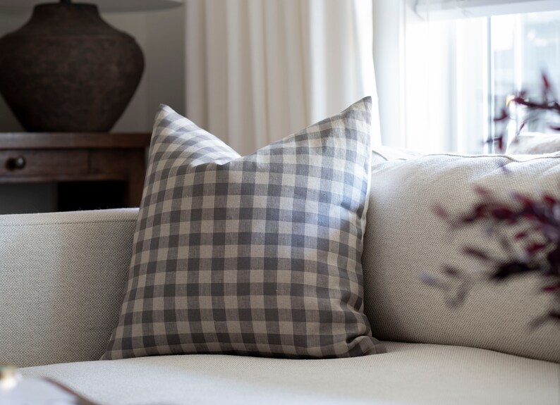 May include: A gray and white gingham throw pillow on a white couch.