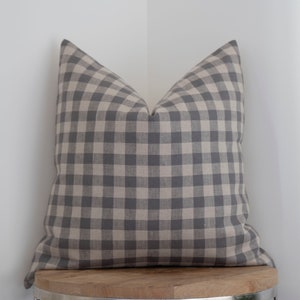 May include: A gray and white gingham pillow on a wooden stool. The pillow is made of a soft, textured fabric.