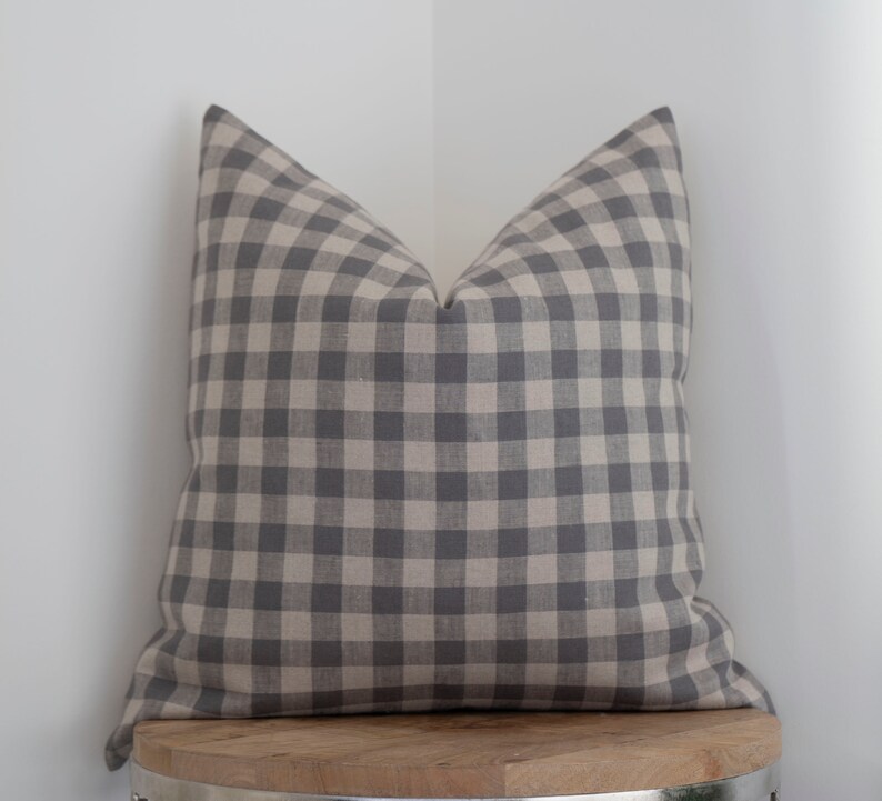 May include: A gray and white gingham pillow on a wooden stool. The pillow is made of a soft, textured fabric.