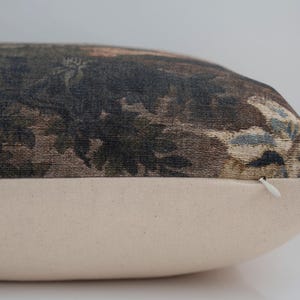 May include: A rectangular decorative pillow with a botanical print in shades of brown, green, and blue. The bottom portion of the pillow is a solid cream color. A white zipper is visible on the side.
