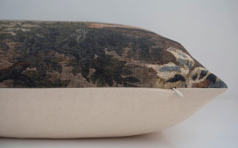May include: A rectangular decorative pillow with a botanical print in shades of brown, green, and blue. The bottom portion of the pillow is a solid cream color. A white zipper is visible on the side.
