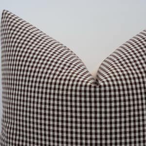 K&ouml;nnte beinhalten: Nahaufnahme eines kissens mit braun-wei&szlig;em Vichy-Muster. Das Kissen hat ein klassisches Karomuster mit hellem Hintergrund und dunkelbraunen Quadraten. Es ist ein dekorativer Artikel f&uuml;r ein Bett oder Sofa.