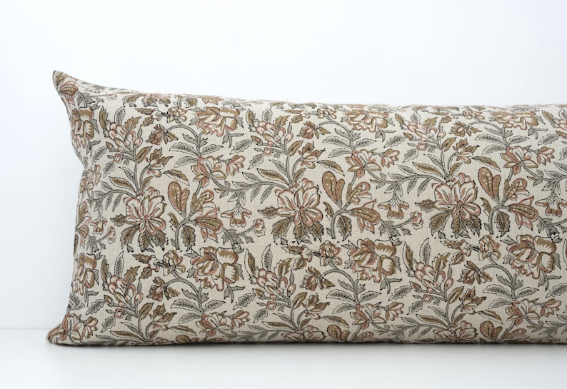 Peut inclure: Un long coussin rectangulaire avec un motif floral. Le coussin pr&eacute;sente un fond cr&egrave;me avec un motif r&eacute;p&eacute;t&eacute; de fleurs marron et roses et de feuilles vertes. C'est un article d&eacute;coratif.