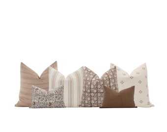 Puede incluir: Una colección de cojines decorativos con varios patrones y colores. Los cojines incluyen diseños a rayas, florales y lisos en tonos neutros de beige, marrón y crema. La disposición sugiere un tema de decoración del hogar.