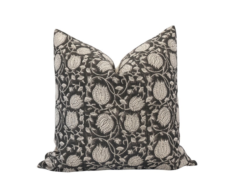 May include: A decorative throw pillow with a dark gray background and a repeating pattern of off-white floral and vine motifs. The pillow has a square shape and is likely made of fabric.