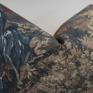 May include: Decorative pillow with a botanical design. The pillow features a detailed pattern of leaves, branches, and flowers in shades of blue, green, brown, and beige. The pillow has a soft, textured appearance, suggesting a comfortable and stylish home decor item.