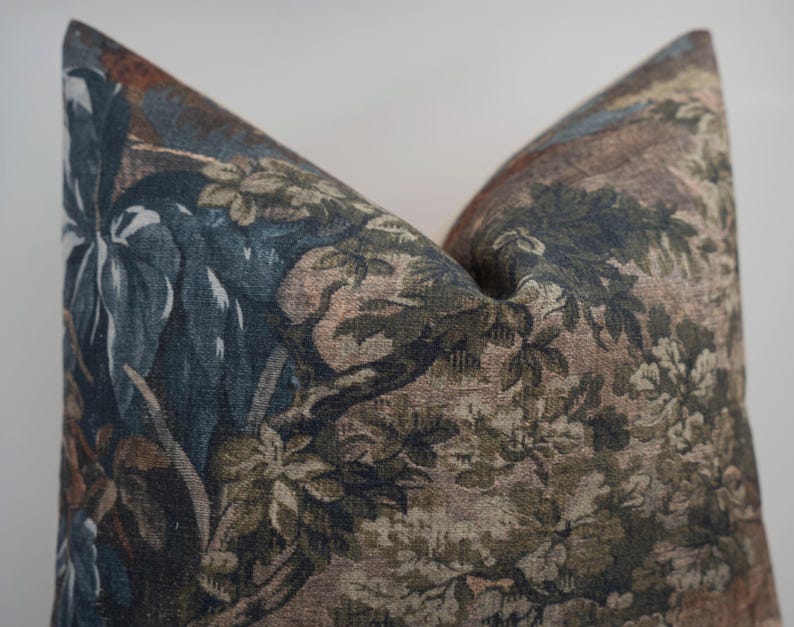 May include: Decorative pillow with a botanical design. The pillow features a detailed pattern of leaves, branches, and flowers in shades of blue, green, brown, and beige. The pillow has a soft, textured appearance, suggesting a comfortable and stylish home decor item.