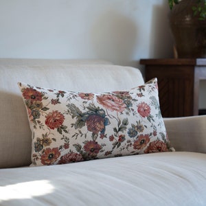 May include: A white linen sofa with a floral patterned cushion. The cushion has a cream background with red, pink, and green flowers.