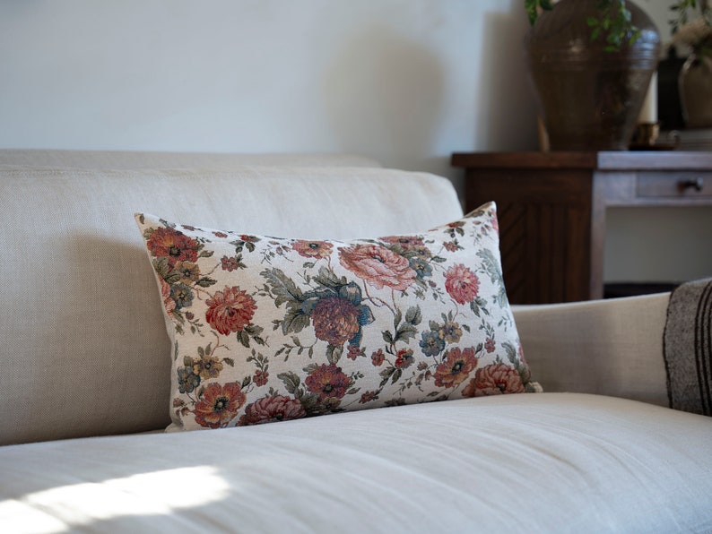 May include: A white linen sofa with a floral patterned cushion. The cushion has a cream background with red, pink, and green flowers.