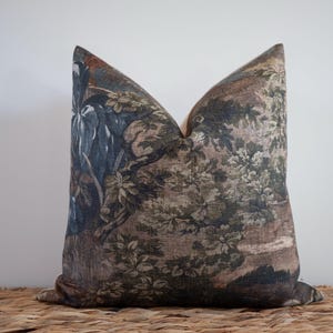 May include: Decorative throw pillow with a vintage-style botanical print in shades of brown, green, and blue. The pillow features a detailed floral and landscape design, adding a touch of classic elegance to home decor.