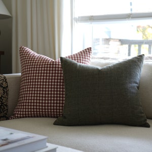May include: Two throw pillows on a white couch. One pillow is red and white gingham, the other is a dark green solid color.