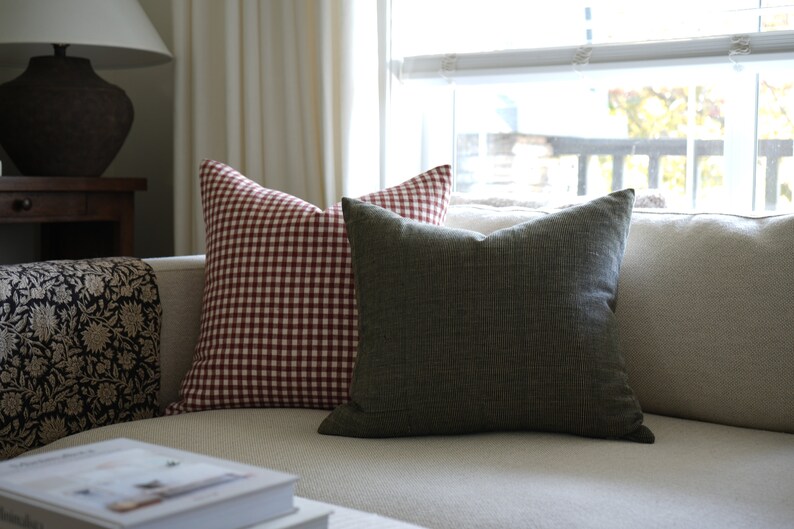 May include: Two throw pillows on a white couch. One pillow is red and white gingham, the other is a dark green solid color.