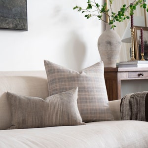 May include: A white linen sofa with two throw pillows, one with a plaid pattern and one with a striped pattern. A brown throw blanket is draped over the back of the sofa.