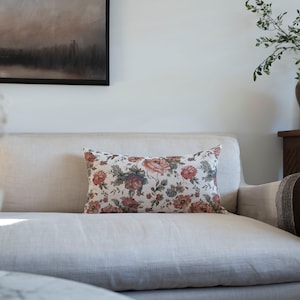 May include: A white linen sofa with a floral patterned cushion. The cushion has a cream background with red, pink, and green flowers.