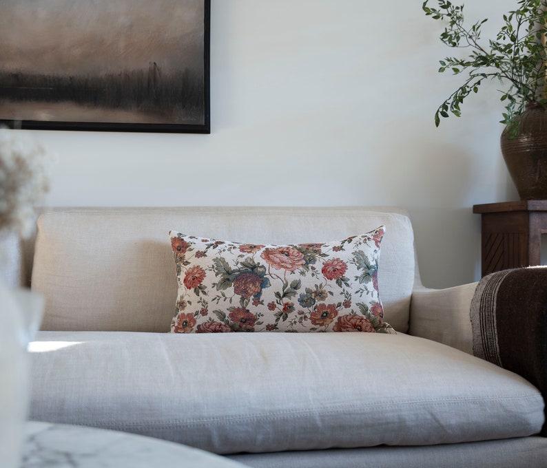 May include: A white linen sofa with a floral patterned cushion. The cushion has a cream background with red, pink, and green flowers.