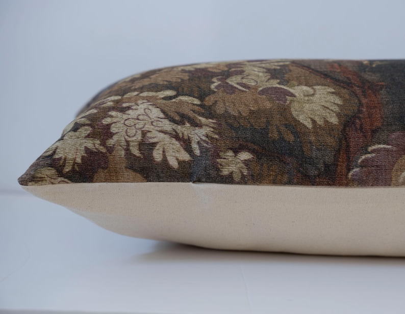 Puede incluir: Un coj&iacute;n rectangular con una base color crema y una parte superior estampada. La parte superior presenta un dise&ntilde;o detallado en tonos de marr&oacute;n, beige y burdeos, que representa un motivo floral o de follaje. El coj&iacute;n es probablemente para la decoraci&oacute;n del hogar.