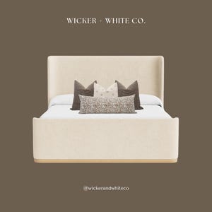 Peut inclure: Un lit rembourr&eacute; beige avec une t&ecirc;te de lit haute et une base en bois. Le lit est orn&eacute; de plusieurs coussins d&eacute;coratifs dans les tons de marron et de cr&egrave;me. Le texte "Wicker + White Co." est en haut.