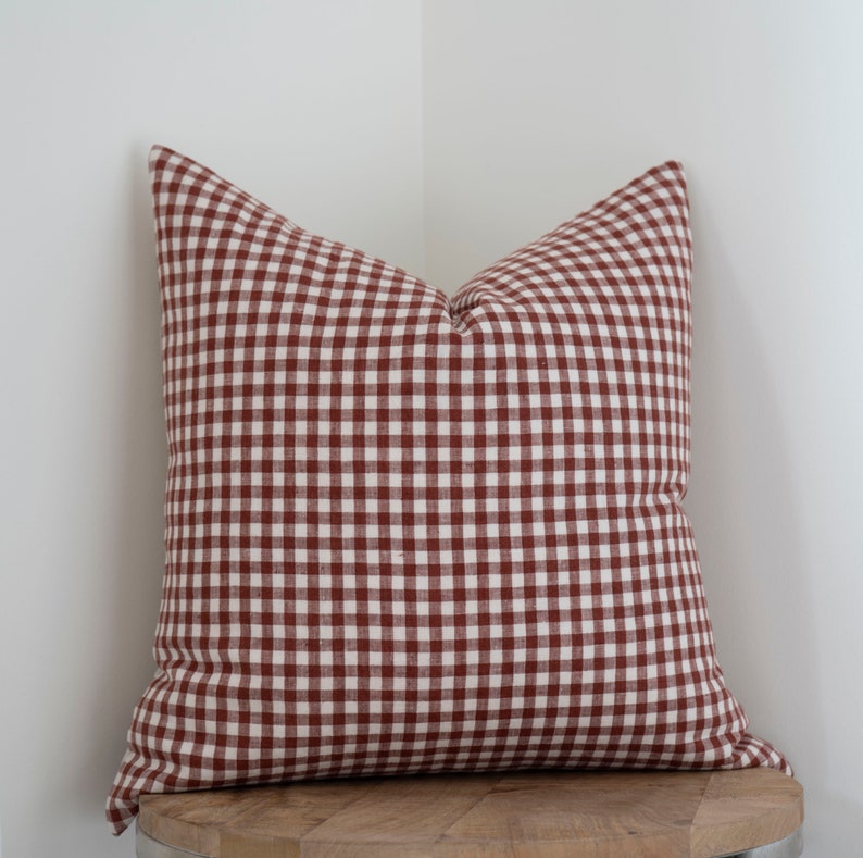May include: A red and white gingham pillow with a square pattern. The pillow is sitting on a wooden surface.