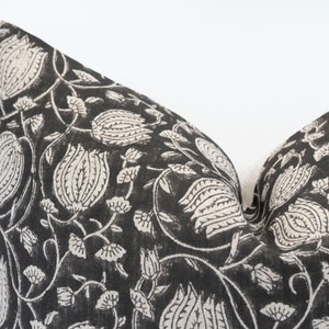May include: A decorative pillow with a black background and a white floral pattern. The pattern includes stylized flowers and vines. The pillow has a soft, textured appearance and is likely made of fabric. The design is repeated across the pillow's surface.