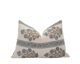 Puede incluir: Un cojín decorativo rectangular con un estampado floral. El cojín presenta un fondo color crema con diseños florales azules y marrones. El diseño incluye un borde con un patrón floral repetitivo.