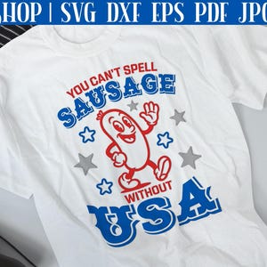 Pode incluir: Camiseta branca com um design gr&aacute;fico vermelho, branco e azul. O gr&aacute;fico apresenta uma salsicha de desenho animado com um rosto sorridente e o texto "You can't spell sausage without USA".