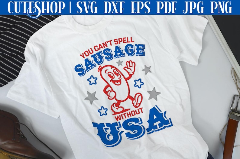 Pode incluir: Camiseta branca com um design gr&aacute;fico vermelho, branco e azul. O gr&aacute;fico apresenta uma salsicha de desenho animado com um rosto sorridente e o texto "You can't spell sausage without USA".