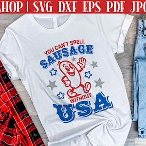 Pode incluir: Camiseta branca com um design gr&aacute;fico vermelho, branco e azul. O gr&aacute;fico apresenta uma salsicha de desenho animado com bra&ccedil;os e pernas, e o texto "You can't spell sausage without USA".