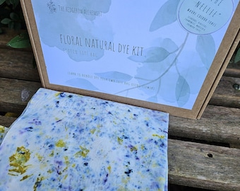 May include: A floral natural dye kit with a cotton tote bag. The kit includes a box with text and a fabric with blue, yellow, and purple floral patterns. The box reads "Floral Natural Dye Kit" and "The Nellie" with "Mauve Colour Tones".