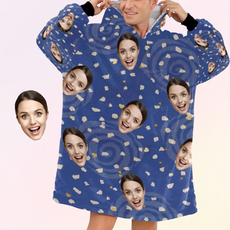 K&ouml;nnte beinhalten: Blauer Kapuzenpullover mit einem sich wiederholenden Muster aus l&auml;chelnden Gesichtern und abstrakten Wirbeln. Die Decke hat eine weiche Textur und eine Kapuze. Das Design umfasst wei&szlig;e und gelbe Akzente. Die Person, die die Decke tr&auml;gt, l&auml;chelt.