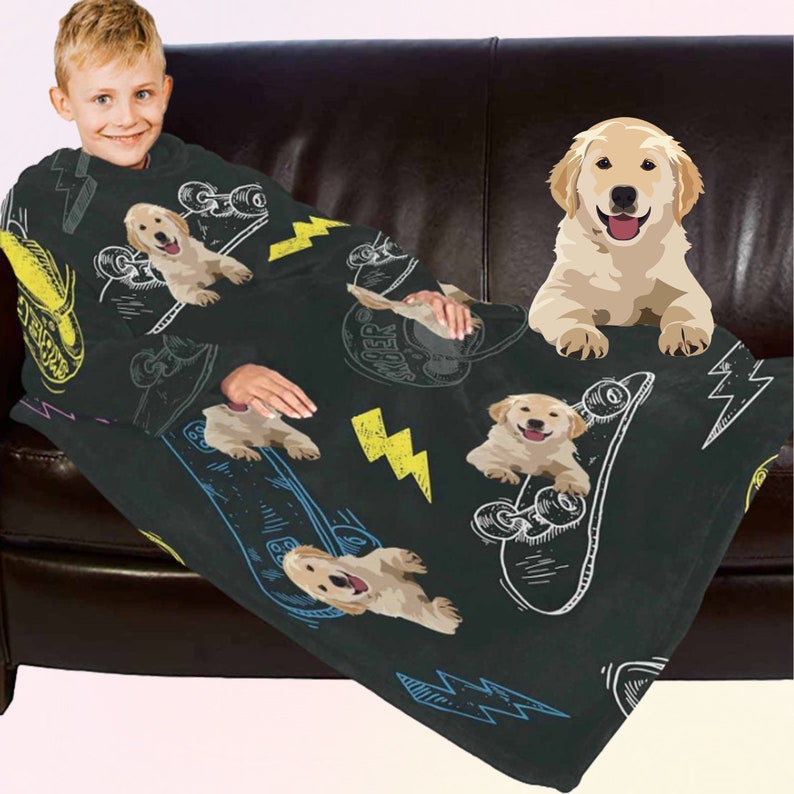 May include: Black wearable blanket featuring a repeating pattern of skateboards, yellow lightning bolts, and cartoon golden retriever puppies. The blanket has sleeves and is designed to be worn. The background is a dark brown couch.