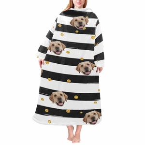 May include: A wearable blanket featuring a repeating pattern of black and white stripes, gold polka dots, and images of a yellow Labrador Retriever's face. The blanket has long sleeves and a hood, designed for comfort and warmth.