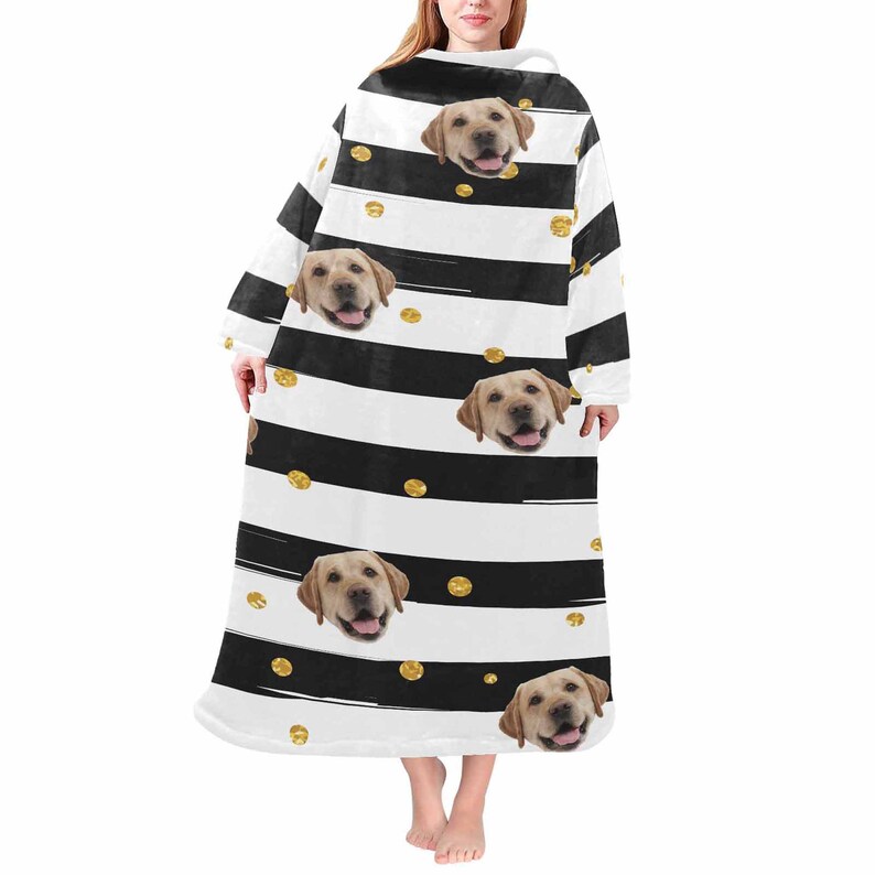 May include: A wearable blanket featuring a repeating pattern of black and white stripes, gold polka dots, and images of a yellow Labrador Retriever's face. The blanket has long sleeves and a hood, designed for comfort and warmth.