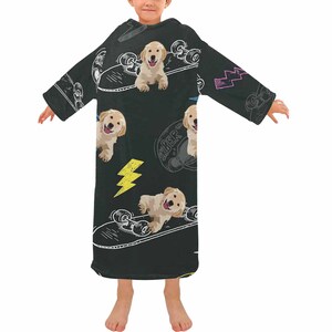 May include: A black wearable blanket featuring a repeating pattern of golden retriever puppies on skateboards, with yellow lightning bolts and the word "Sk8er" in a circle. The blanket has long sleeves and a hood.