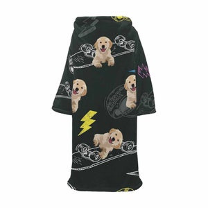 May include: Black wearable blanket featuring a repeating pattern of golden retriever puppies, skateboards, and yellow lightning bolts. The blanket has a hood and sleeves, perfect for lounging. The word "SK8ER" is visible on the skateboard.