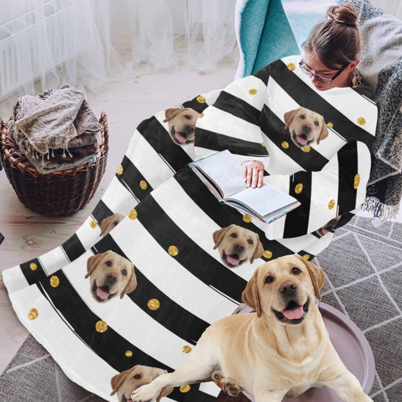 May include: A black and white striped blanket with gold polka dots and images of a yellow Labrador Retriever. The blanket is draped over a person sitting in a chair, and a dog is lying on the floor.