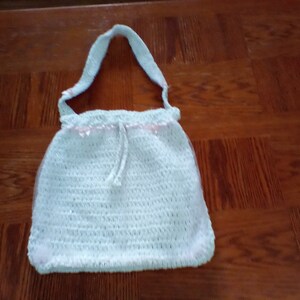 May include: A light blue crocheted tote bag with a pink ribbon trim and a drawstring closure.