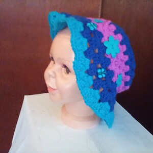 Könnte beinhalten: Ein blauer, rosa und türkisfarbener gehäkelter Sonnenhut mit blauen Blumenverzierungen.