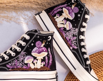 May include: Black high-top sneakers with embroidered purple mushrooms and floral designs. The sneakers have white laces, soles, and toe caps. The design includes a snail on top of a mushroom.