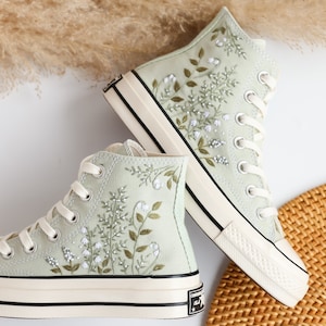 May include: A pair of light green high-top canvas sneakers with white laces and a floral embroidery design. The sneakers have a white rubber sole with a black stripe.