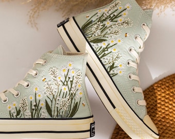 Puede incluir: Zapatillas altas de color verde claro con bordados de margaritas blancas con centros amarillos y tallos verdes. Las zapatillas tienen cordones blancos, puntera color crema y una franja negra a lo largo de la suela. Miden unos 25 cm.