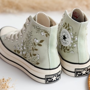 Op de afbeelding: Een paar lichtgroene hoge canvas sneakers met witte veters en een zwart sterlogo. De sneakers hebben een geborduurd bloemenpatroon.