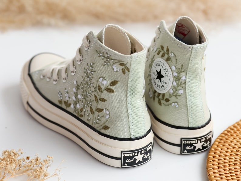 Op de afbeelding: Een paar lichtgroene hoge canvas sneakers met witte veters en een zwart sterlogo. De sneakers hebben een geborduurd bloemenpatroon.
