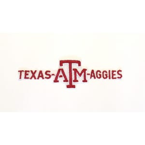 Könnte beinhalten: Ein rechteckiger gestickter Aufnäher mit dem Text TEXAS-A&M-AGGIES in rotem Garn. Das zentrale A&M-Logo ist deutlich hervorgehoben, wobei die Buchstaben A und M ineinander verschlungen sind, flankiert von den Wörtern TEXAS und AGGIES.