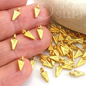 Puede incluir: Un montón de abalorios triangulares de metal dorado con un bucle en la parte superior. Los abalorios miden aproximadamente 2,5 cm de largo y tienen una superficie texturizada.
